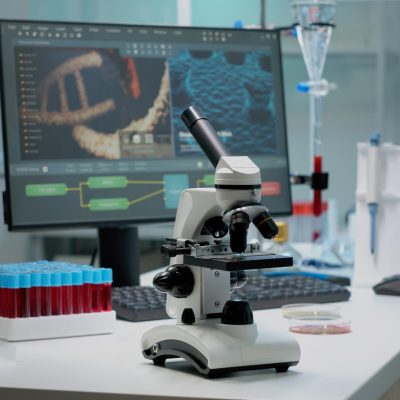 Scientific microscope on laboratory desk with researching instruments at professional workplace. Close up of investigation tool with glass lens for chemical substance lab examination